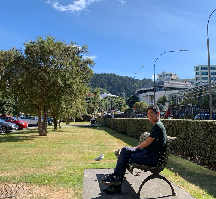 Youngsoo Kim sits on a bench outside on a sunny day.