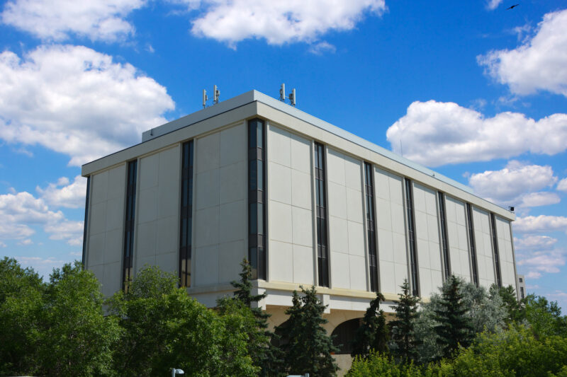 A photo taken from ground level looking up at the Archer Library. Trees are in the foreground and the sky is blue with white clouds.